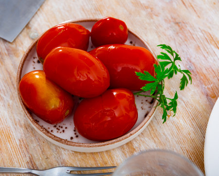 Homemade savory pickled tomatoes served on plate with fresh greensの写真素材