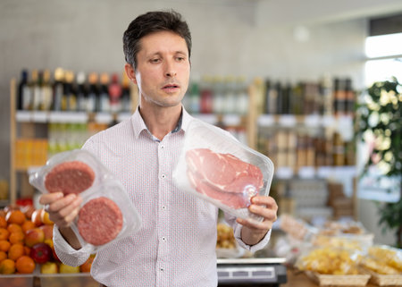 Man in light shirt choose and buy raw cooled beef entrecote and hamburger cutlet in storeの写真素材