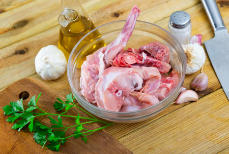 Raw sliced rabbit in glass bowl with greens, garlic, oil and spicesの写真素材