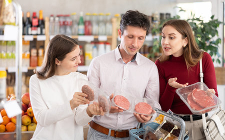 Family with teenage girl choosing hamburger or beef entrecote in groceryの写真素材
