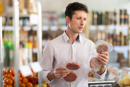 Man in light shirt choose and buy raw cooled semi-finished hamburger cutlet in storeの写真素材