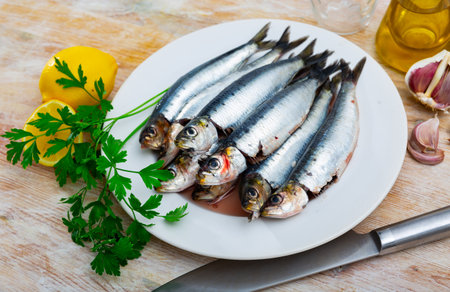 Sardines lying on white plate with lemon, parsley and garlicの写真素材