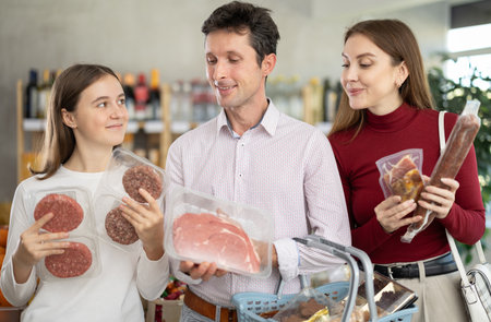 Dad, mom and daughter choose raw meat product and dry sausage in shopの写真素材