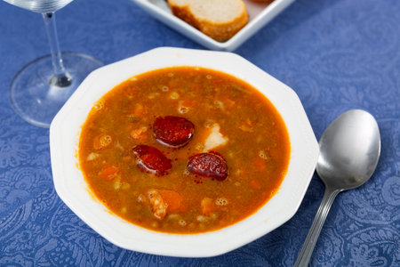 Spicy stewed lentils with suasage and vegetables with thick tomato sauce served in white plate. Spanish cuisineの写真素材