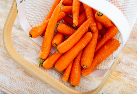 Raw carrots in bucket on wooden tableの写真素材