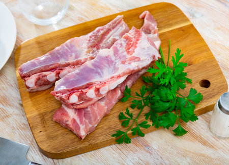 Fresh meaty pork ribs with condiments ready for cooking on wooden cutting boardの写真素材