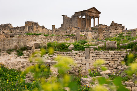 View of weathered remains of Capitol Temple in Dougga, historic Roman archaeological site in Tunisia, with iconic columns and pediment, under clouded spring sky..の写真素材