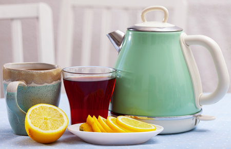 Electric kettle, two cups with tea and sliced lemonの写真素材
