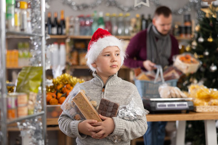 Little boy holding turrons and other sweets in market with Xmas decorationの写真素材