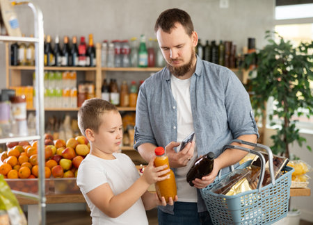 European man with son customer at shop scans QR code on juice bottle using phone cameraの写真素材