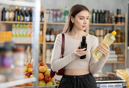 Young woman choosing olive and sunflower oil in groceryの写真素材