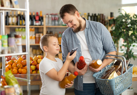 European man with son customer at shop scans QR code on juice bottle using phone cameraの写真素材