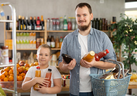 Man with son hold packages plastic bottle and choose consider fruit juice in storeの写真素材