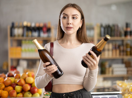 Girl hold packages bottle tin and choose consider beer in storeの写真素材