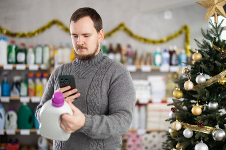 Middle-aged man scanning QR-code on detergent in store during Christmasの写真素材