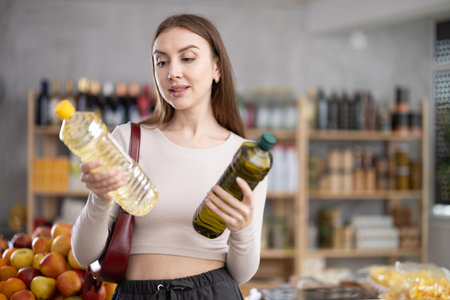 Young woman choosing olive and sunflower oil in groceryの写真素材