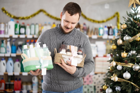 Young man choosing Christmas gift set with self-care products in storeの写真素材