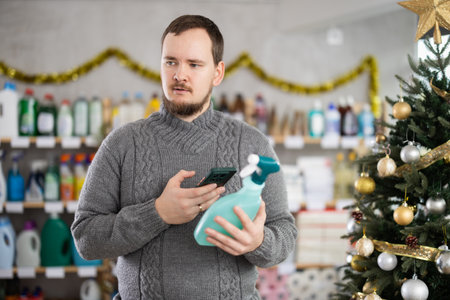 Man scanning cleaning spray bottle with phone in festively decorated storeの写真素材