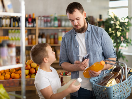 European man with son customer at shop scans QR code on drink bottle using phone cameraの写真素材