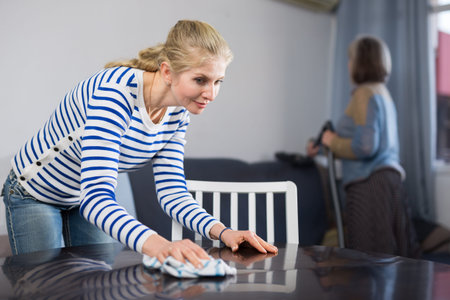 Adult daughter and her mature mother clean the room