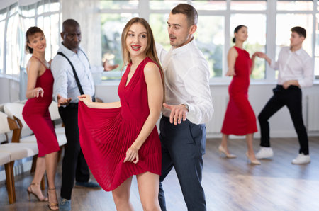Happy young Woman in red dress with man practising charleston dancing in dance hall