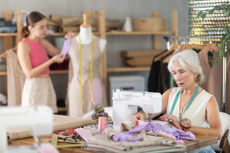 Elderly woman sews on machine female assistant sews on mannequin