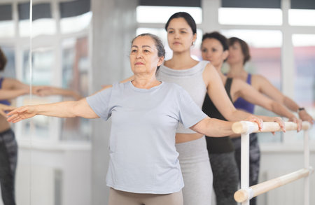 Women of different ages exercise near the ballet barre at group training session