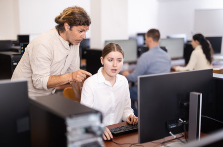 Adult male teacher helps woman work on computerの写真素材