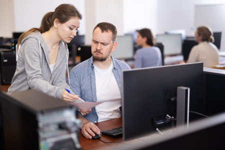 Female teacher helps man student complete difficult task at PC, show document
