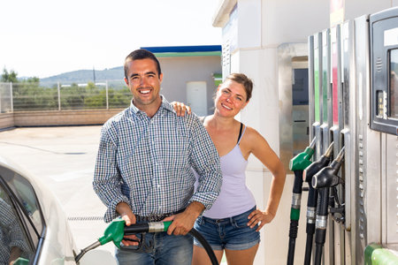 Positive couple filling up tank of their car with gasoline in gas station