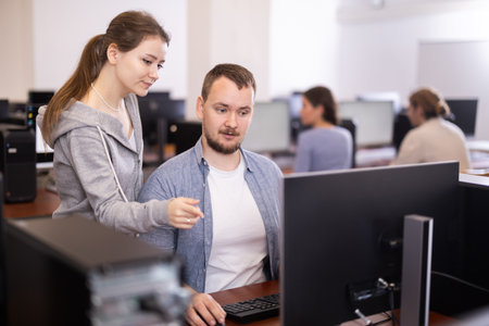 Female teacher helps man with learning on computer in university computer labの写真素材