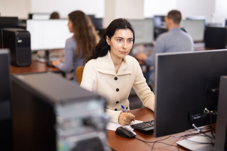 Young woman student looks at monitor screen, write down note in notebook