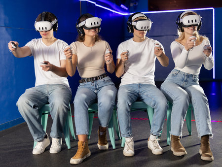 In darkened hall of gaming club, four friends in VR helmet takes part in group gameの写真素材