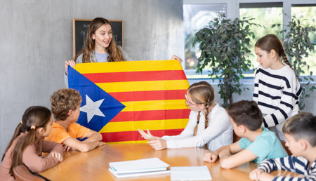 Geography lesson in school class - teacher talks about Catalonia, holding flag in his hands
