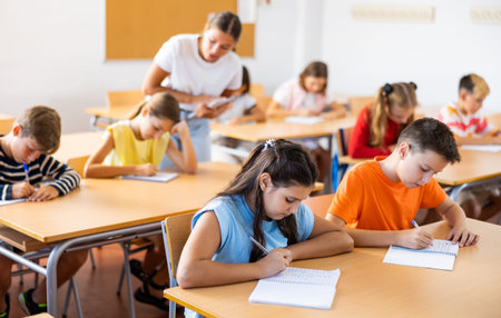 Diligent tweens listening to lecture of teacher and writing in notebooks