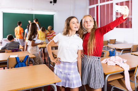 Cheerful girls classmates taking funny selfie with phone during breakの写真素材