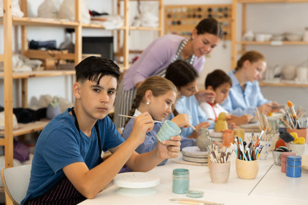 Teenage boy painting ceramic cupin pottery workshop