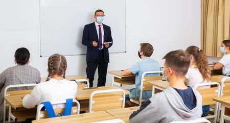 Male teacher in mask lecturing to teenagers