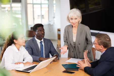 Senior woman head of department speaks at meeting and reports unpleasant news to frowning colleagues