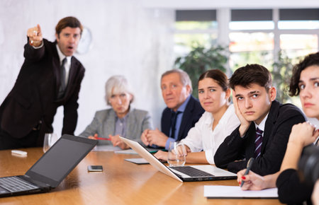 Frustrated guy sitting in office with coworkers and irritated boss