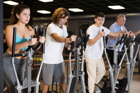 Group of people of different ages train on elliptical trainers steppers