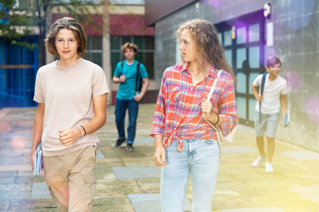 Smiling teenagers boy and girl walking home after finishing college lessons on day