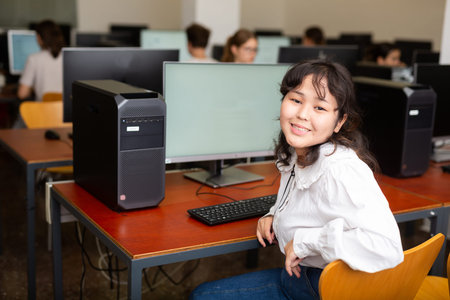 Portrait of fifteen-year-old schoolgirl studying at computer in class at an informatics lesson with...