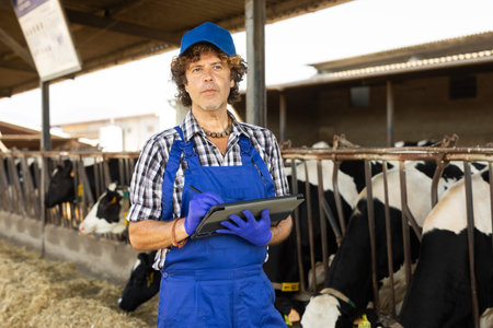 Middle-aged male vet checking cows with tablet at dairy farm