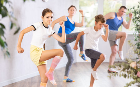 Friendly sporty parents with teen daughter and son learning new active dynamic dance in wellness...