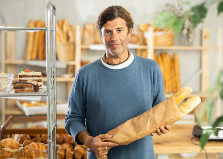 Portrait of male customer holding paper bag of baguettes in bakery interior