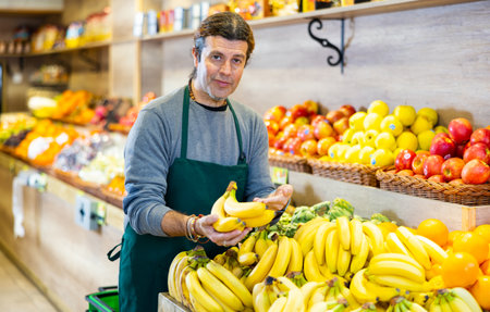 Positive male seller with ripe bananas on supermarketの写真素材