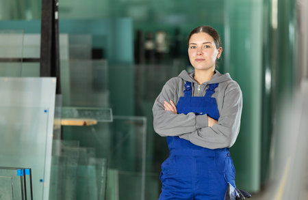 Girl glazer employee in blue overall works in glass processing shopの写真素材