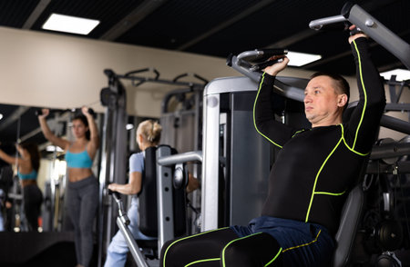 Sporty male athlete using overhead press machine in gym