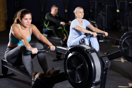 Young girl exercising on rowing machine during workout in gym